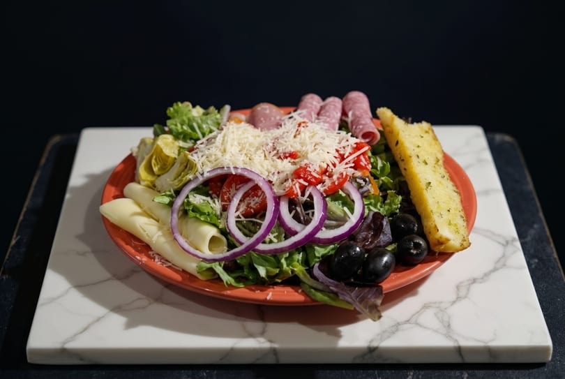 Antipasto salad with salami, cheese, olives, artichokes, and garlic bread on a red plate.
